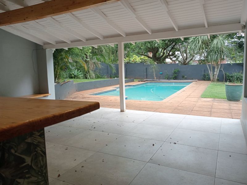 Covered patio area featuring a built-in bar counter, overlooking a private swimming pool and garden space.