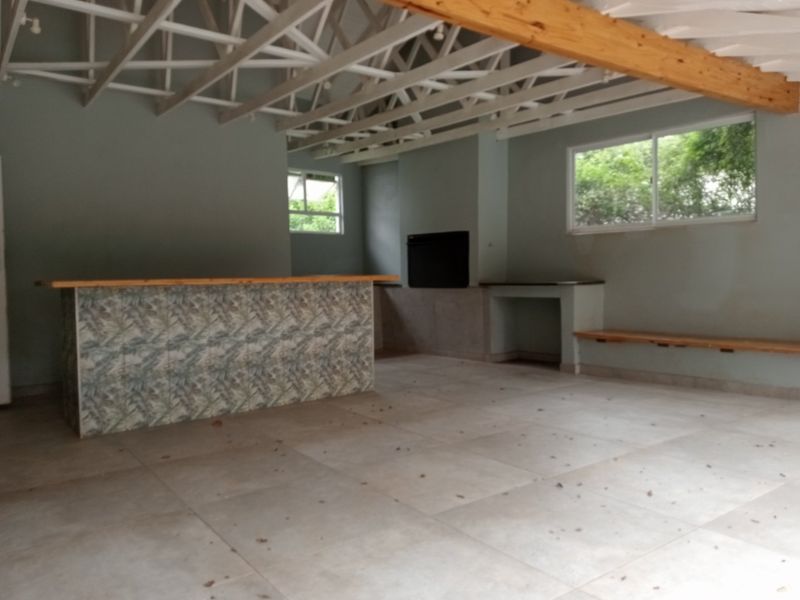 Spacious entertainment area featuring a built-in bar, fireplace, exposed roof trusses, and tiled flooring, offering a versatile space for social gatherings.