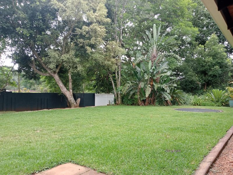A well-maintained private garden featuring a lush green lawn, mature trees, and a solid boundary wall.