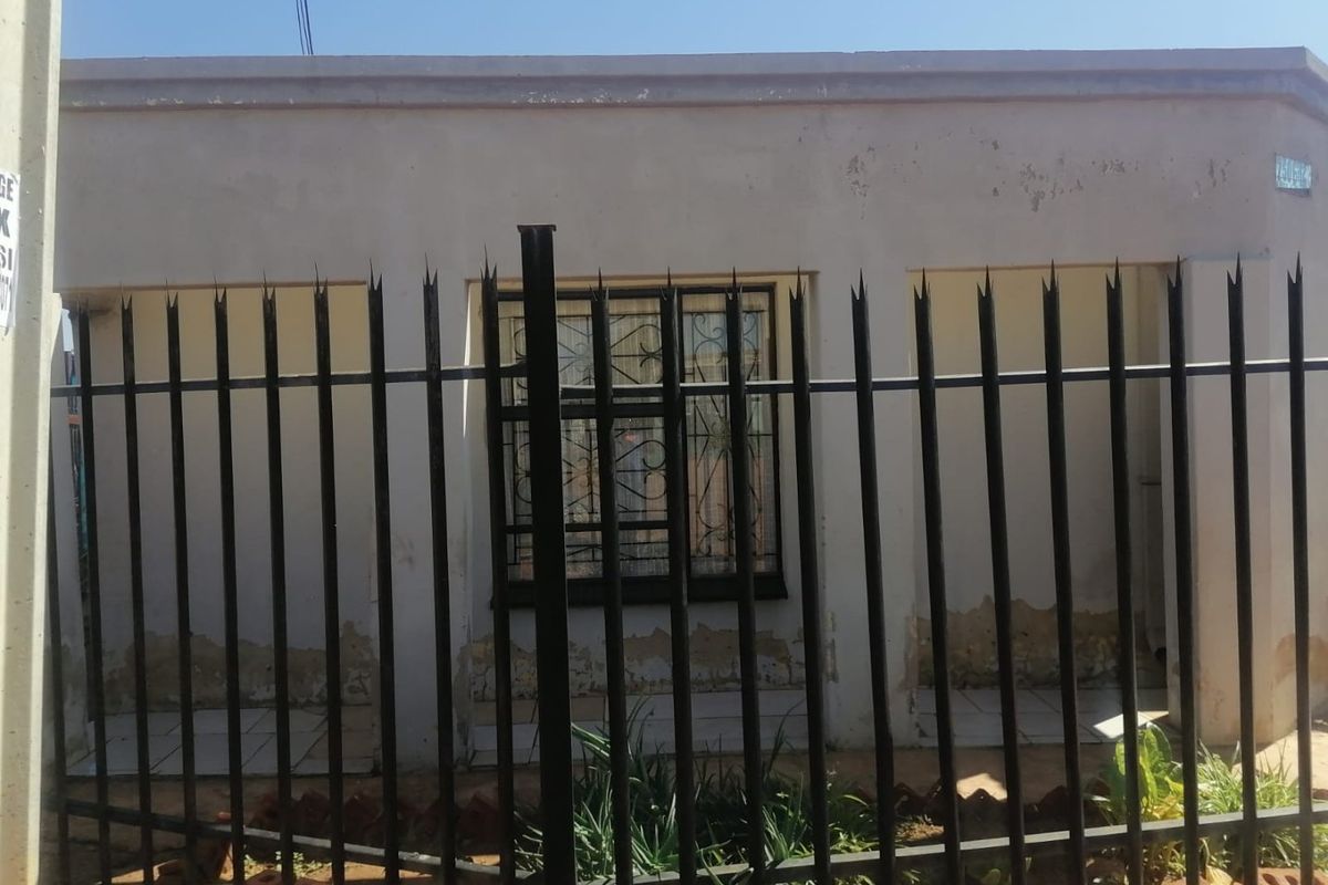 Front elevation of a residential property featuring security fencing and window bars, showing significant wear to the exterior wall finish.