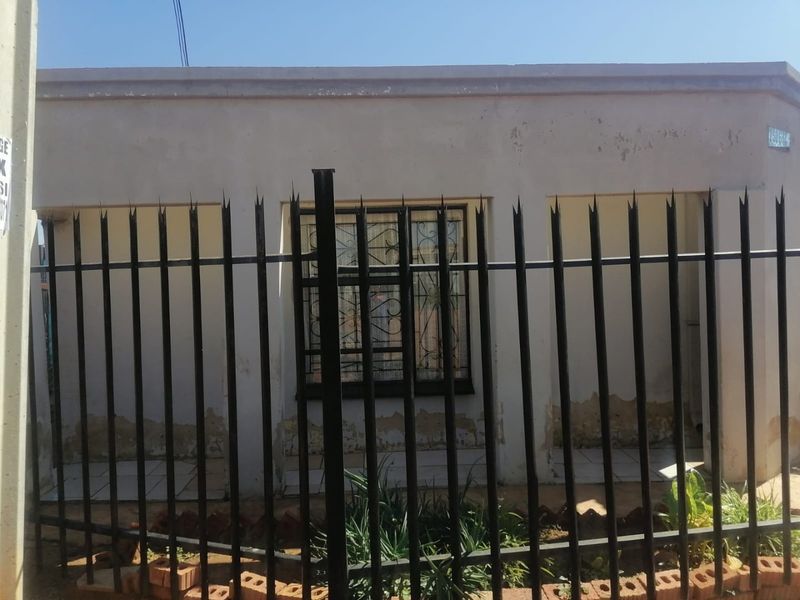 Front elevation of a residential property featuring security fencing and window bars, showing significant wear to the exterior wall finish.