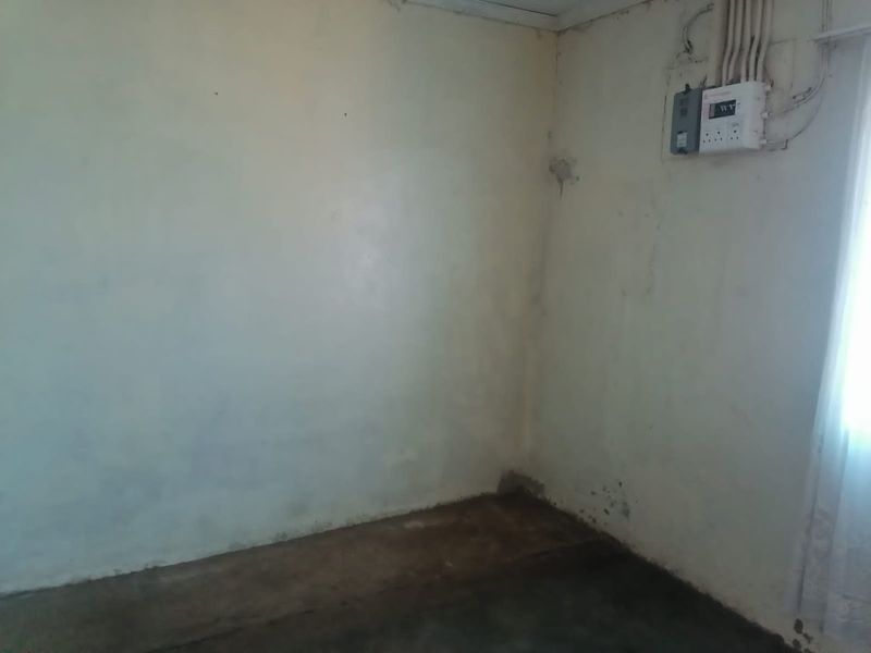 An empty utility space featuring an exposed electrical distribution board, showing significant wear to the wall and floor surfaces.
