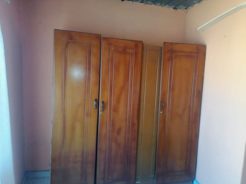 A bedroom featuring built-in wooden cupboards, requiring cosmetic updates to the ceiling and wall finishes.