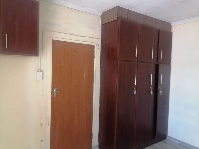 A bedroom featuring built-in dark wood cupboards and overhead storage, requiring cosmetic updates to the walls and ceiling to improve the overall condition.