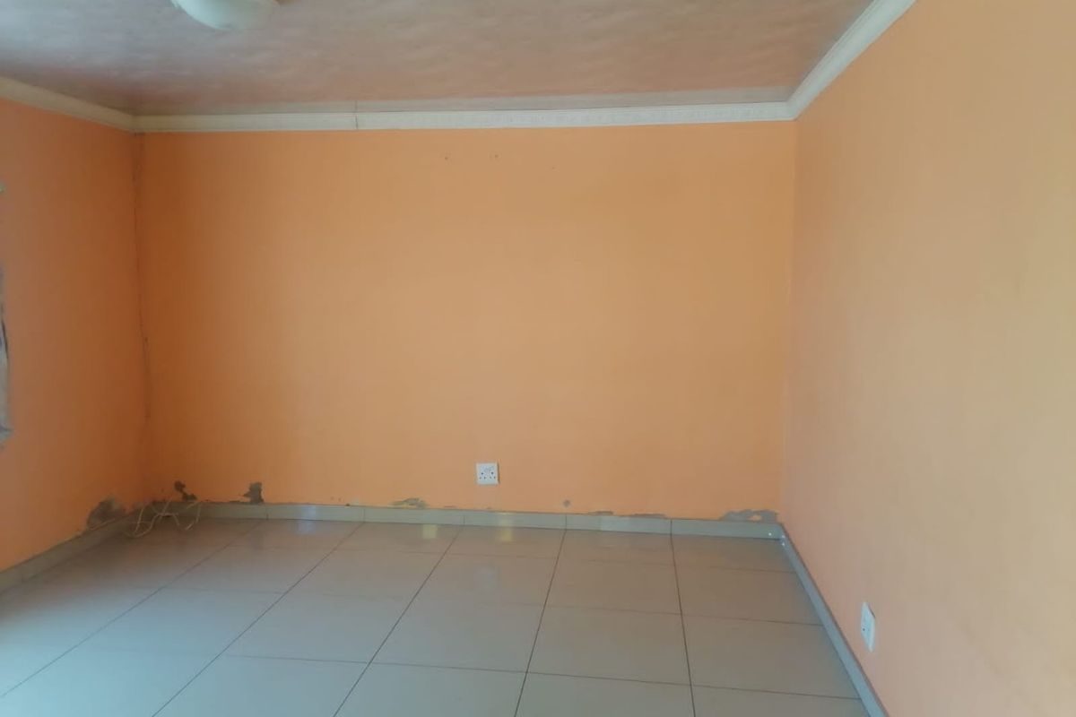 An empty bedroom featuring tiled flooring and peach-colored walls with visible signs of wear and paint damage near the baseboards.