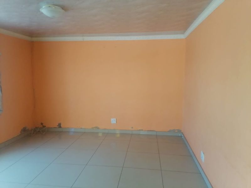 An empty bedroom featuring tiled flooring and peach-colored walls with visible signs of wear and paint damage near the baseboards.