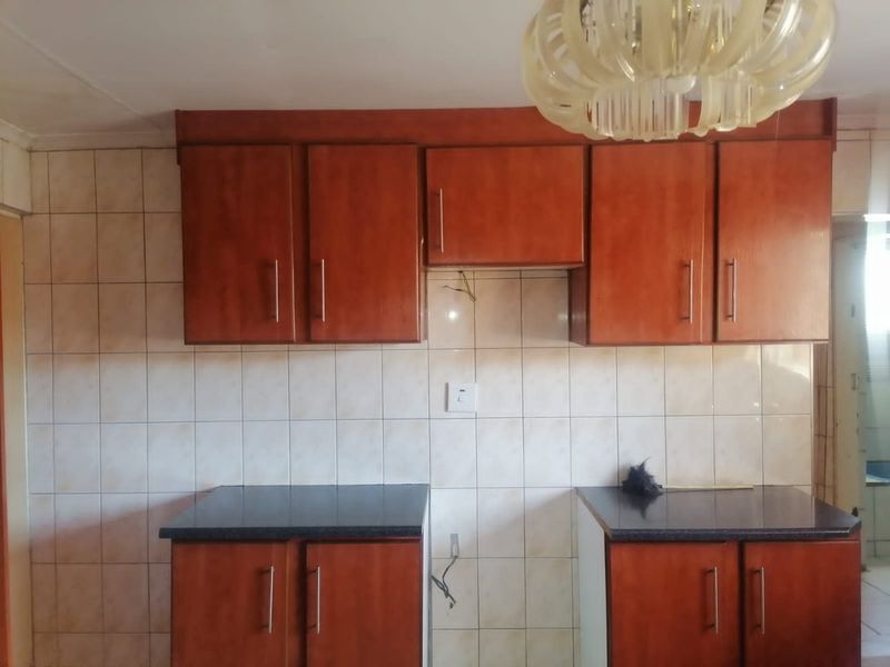 A dated kitchen area featuring wood-finish cabinetry, dark countertops, and tiled walls, currently vacant and requiring minor electrical and cosmetic updates.