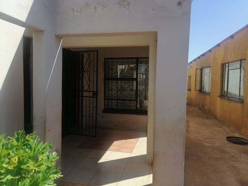 A covered patio area featuring tiled flooring, security gate, and security bars on the windows, requiring exterior maintenance and paint touch-ups.