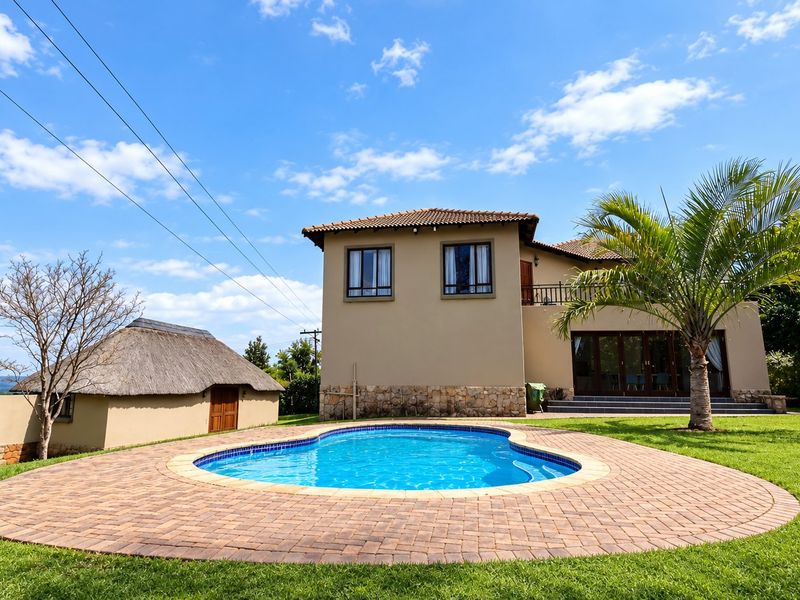 A well-maintained farm property featuring a swimming pool with a paved deck, a separate thatched outbuilding, and a two-story residence with a balcony.