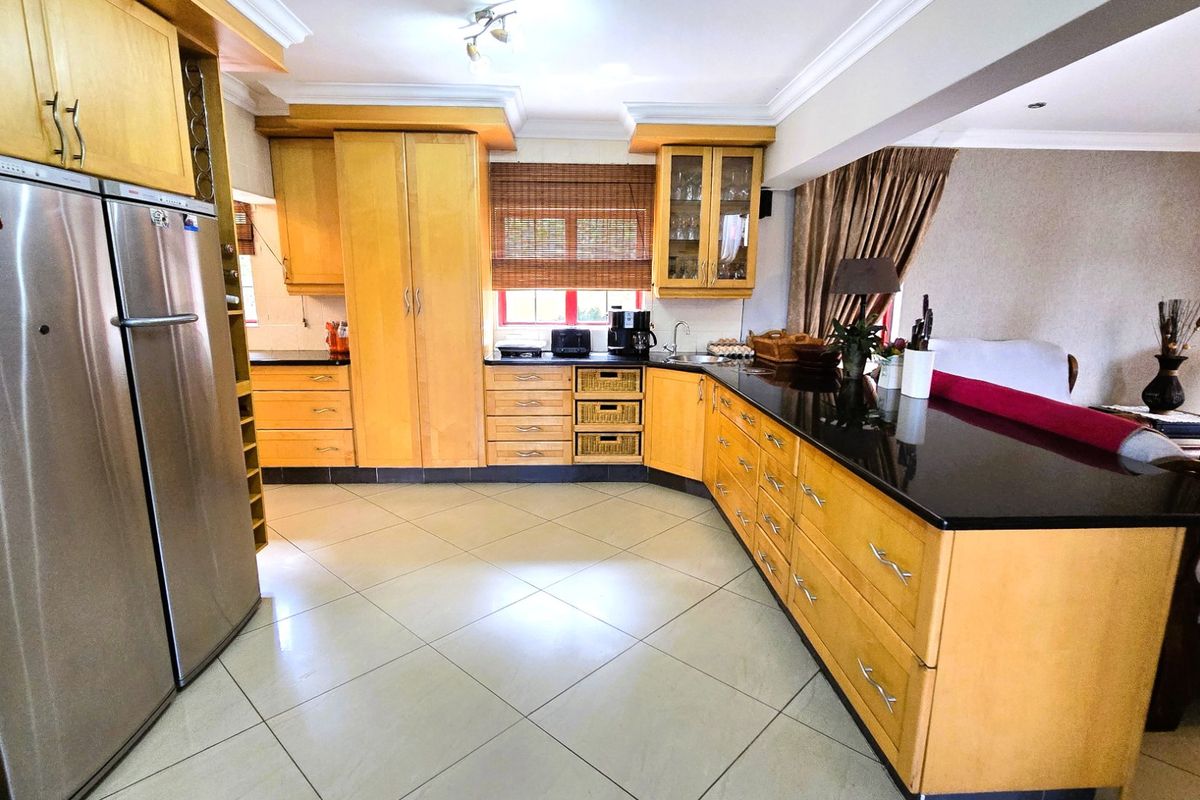 Spacious kitchen featuring light wood cabinetry, black granite countertops, tiled flooring, and integrated storage solutions, seamlessly flowing into the adjacent living area.