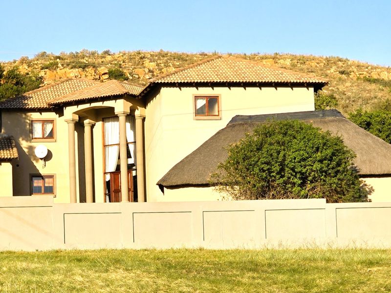 A multi-level farm residence featuring a combination of tiled and thatched roofing, prominent entrance columns, and a secure boundary wall.