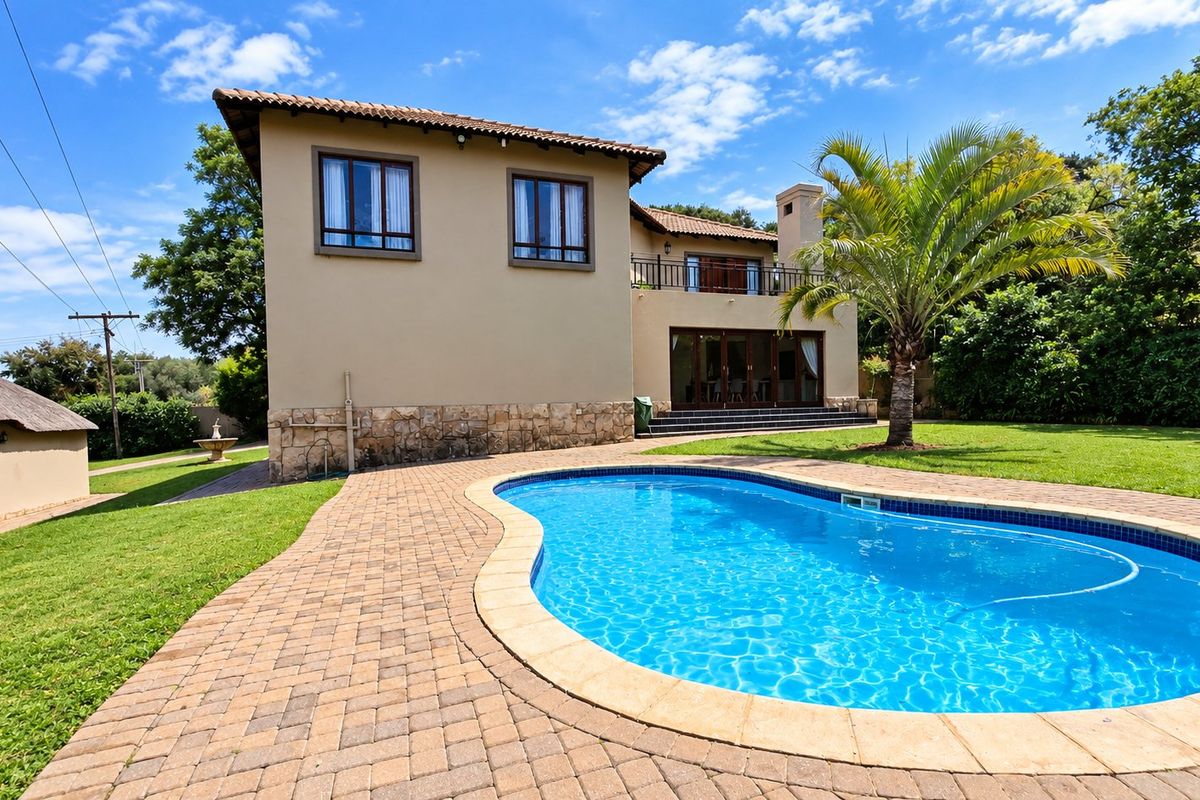 Rear view of a two-story farm-style residence featuring a swimming pool, paved patio area, stone-clad base, and an upper-level balcony.