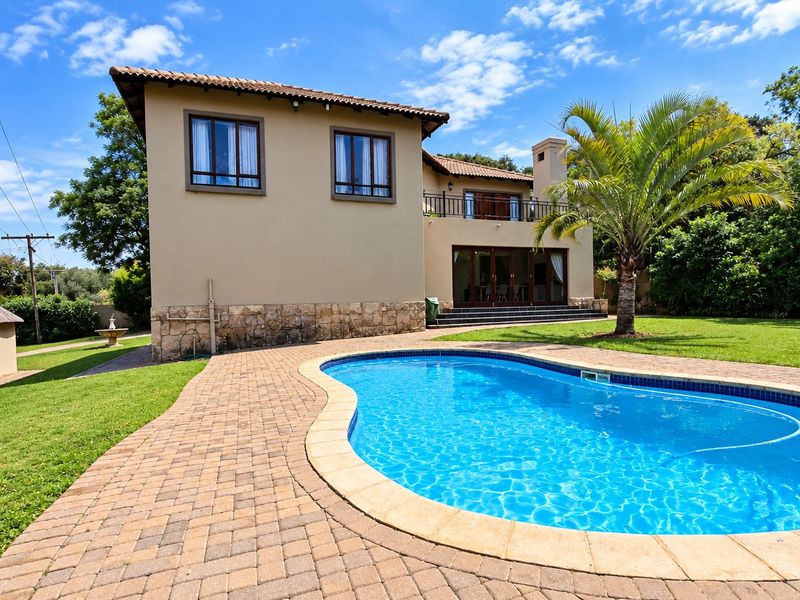 Rear view of a two-story farm-style residence featuring a swimming pool, paved patio area, stone-clad base, and an upper-level balcony.