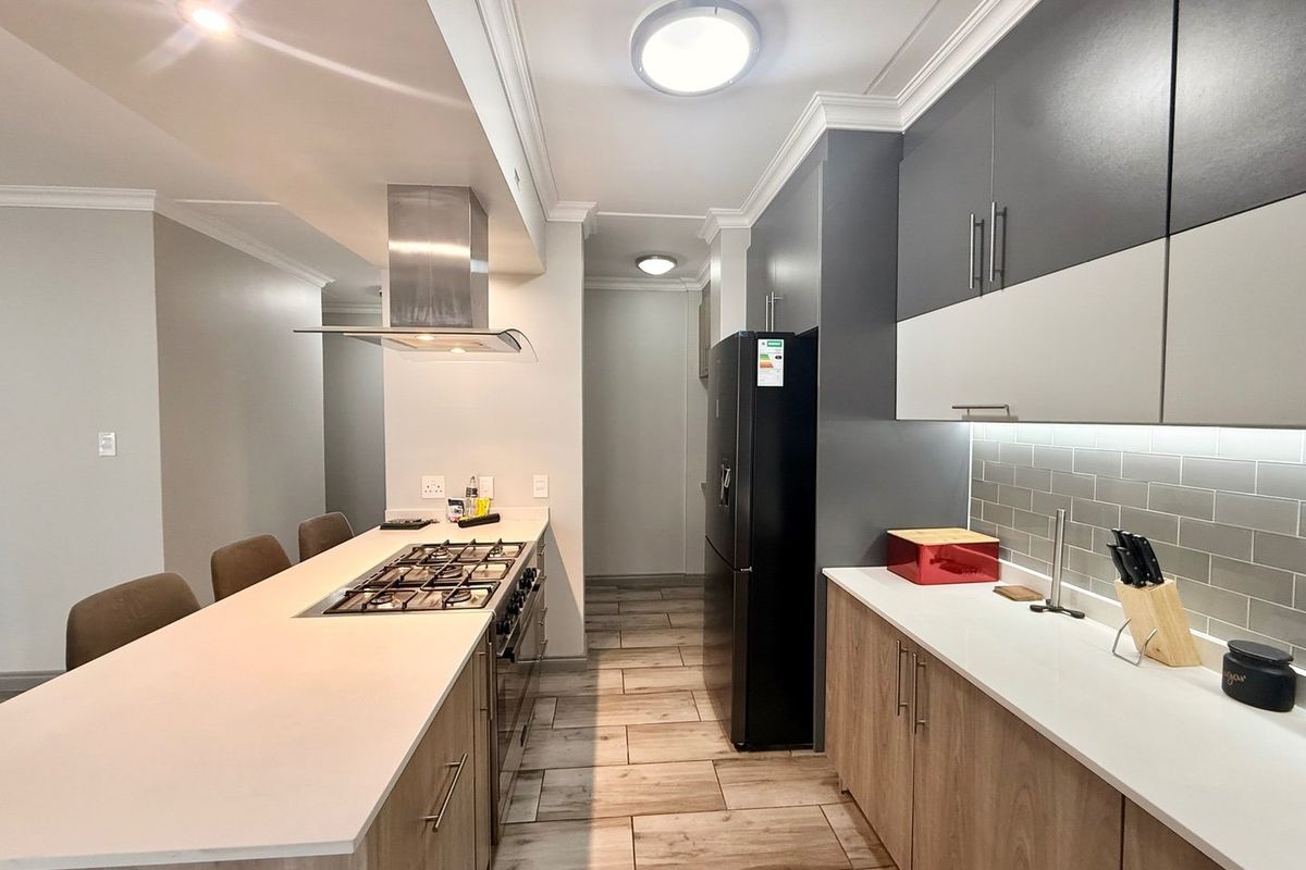 Modern kitchen featuring a central island with a gas hob, sleek two-tone cabinetry, stone countertops, and a stylish subway tile backsplash.