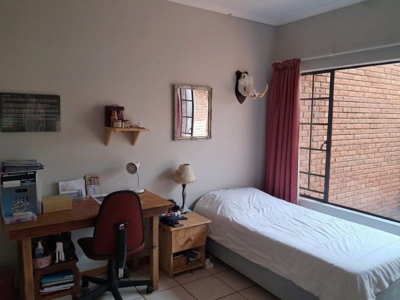 A functional bedroom featuring tiled flooring and a large window fitted with security bars, providing natural light.
