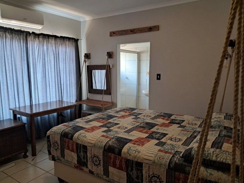 A bedroom featuring tiled flooring, a wall-mounted air conditioning unit, and direct access to an en-suite bathroom.