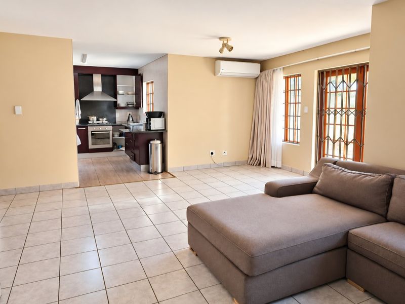 Open-plan living area featuring tiled floors, a split-system air conditioner, and an adjoining kitchen with built-in cabinetry, oven, and extractor fan.