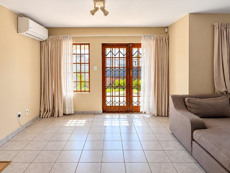 A bright living room featuring tiled flooring, a split-system air conditioner, and secure timber-framed glass doors leading to the exterior.