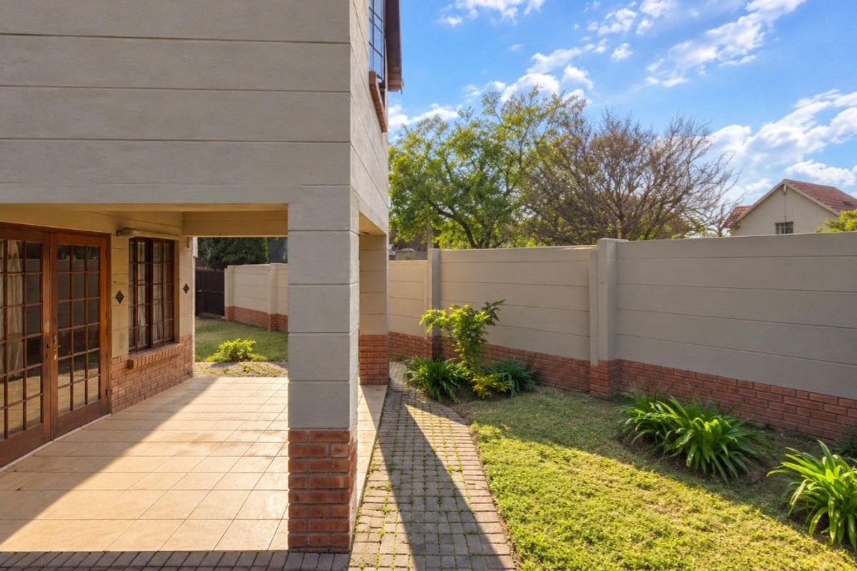 A well-maintained rear exterior featuring a covered patio, paved walkway, and a private garden enclosed by a perimeter wall.