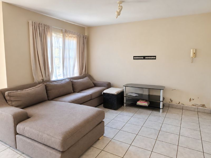 A living room featuring tiled flooring and a wall-mounted intercom, currently showing signs of wall surface damage and peeling paint.