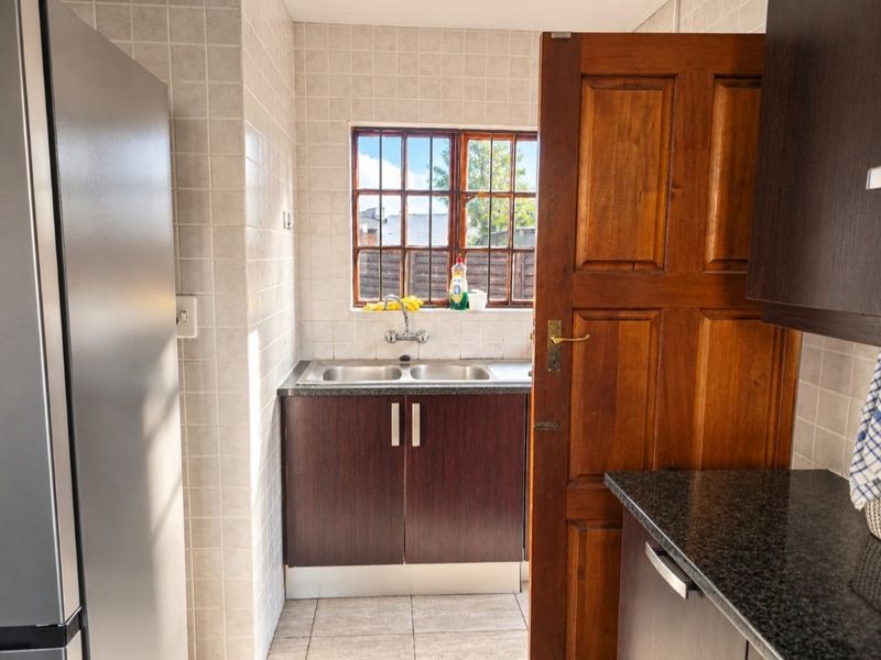 A functional kitchen area featuring dark laminate cabinetry, granite countertops, a double bowl stainless steel sink, and tiled wall finishes.