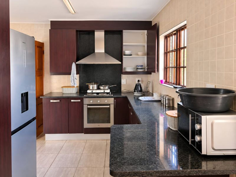 A functional kitchen featuring dark wood cabinetry, granite countertops, a built-in oven with gas hob, and a tiled backsplash.