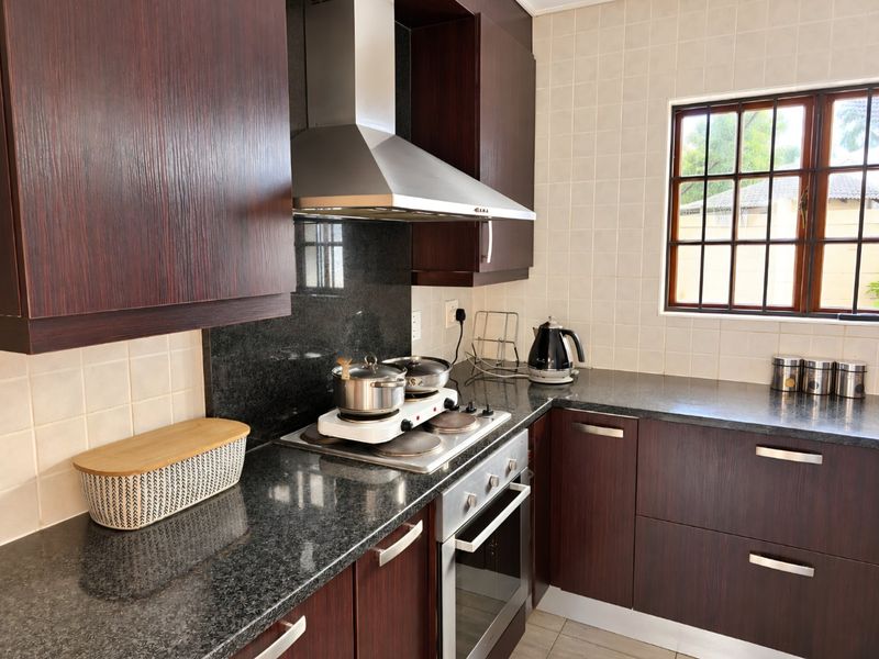 A functional kitchen featuring dark wood cabinetry, granite countertops, a stainless steel extractor fan, and a built-in oven with an electric hob.