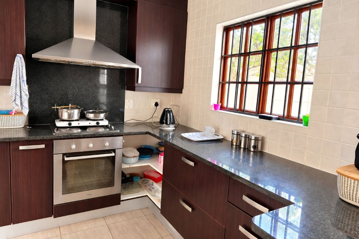 A functional kitchen featuring dark wood cabinetry, granite countertops, a built-in oven with gas hob, and a tiled backsplash with a window view.