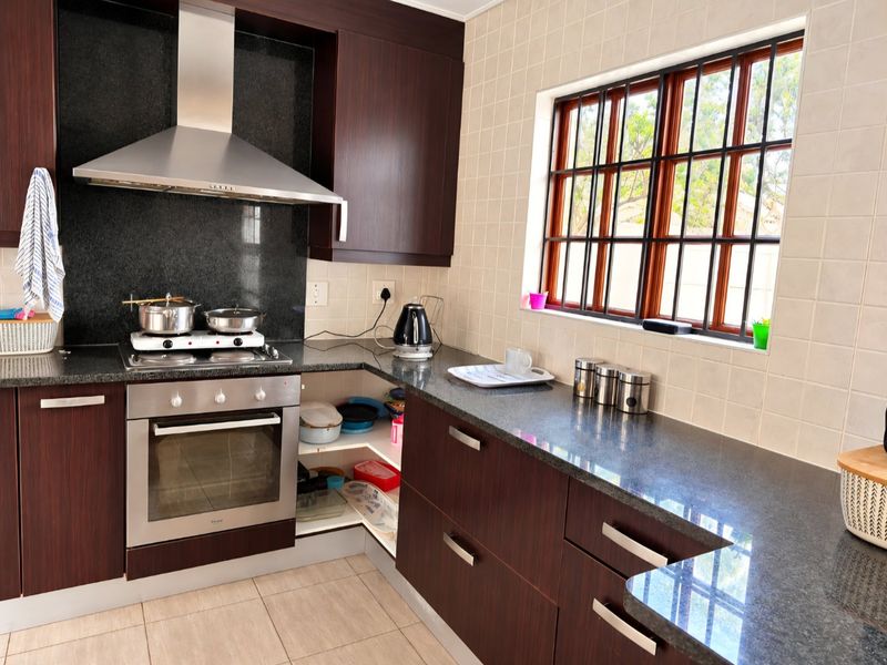 A functional kitchen featuring dark wood cabinetry, granite countertops, a built-in oven with gas hob, and a tiled backsplash with a window view.