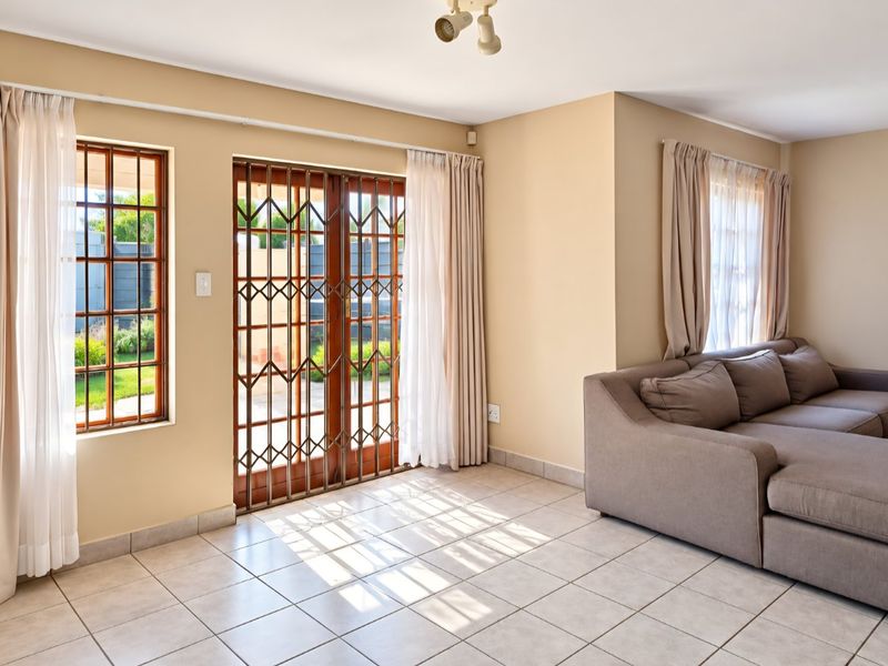 Bright living room featuring tiled flooring, timber-framed windows, and a security gate leading to the outdoor area.