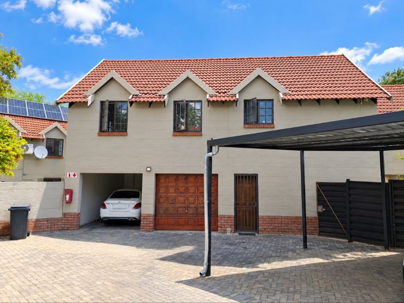 Front elevation of a townhouse featuring a tiled roof, paved driveway, integrated garage, and a covered carport area.