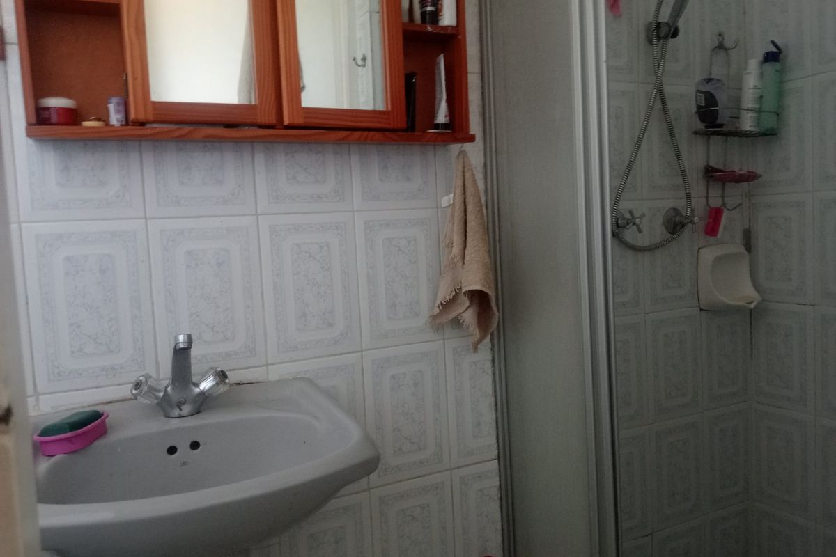 A functional bathroom featuring a pedestal basin, wall-mounted medicine cabinet, and a shower enclosure with tiled walls.