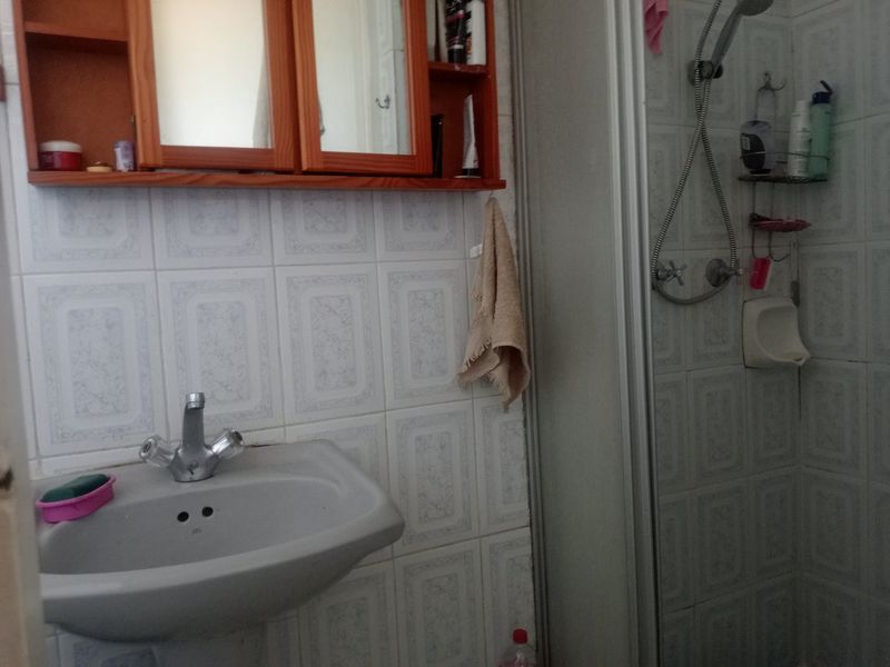 A functional bathroom featuring a pedestal basin, wall-mounted medicine cabinet, and a shower enclosure with tiled walls.