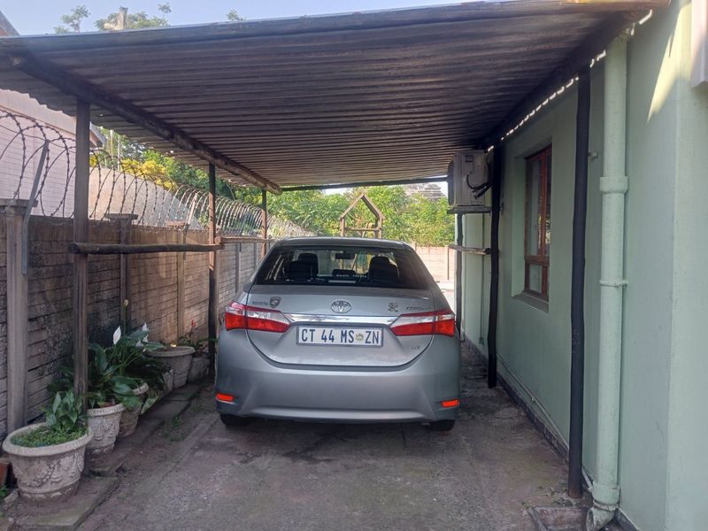 A covered carport area featuring a corrugated metal roof, concrete flooring, and perimeter security fencing.
