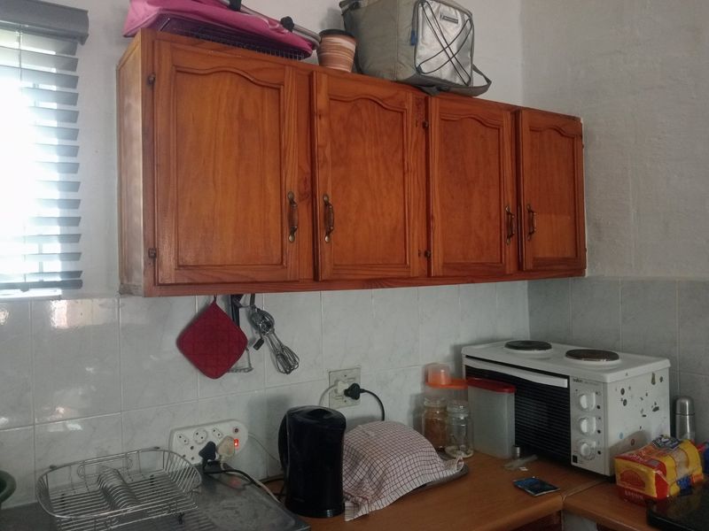 A functional kitchen area featuring wooden wall-mounted cabinetry, a tiled backsplash, and laminate countertops, providing essential storage and workspace.