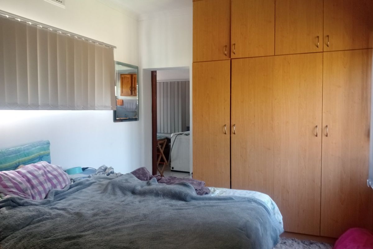 A bedroom featuring floor-to-ceiling built-in wooden cupboards and vertical window blinds, offering functional storage and natural light control.