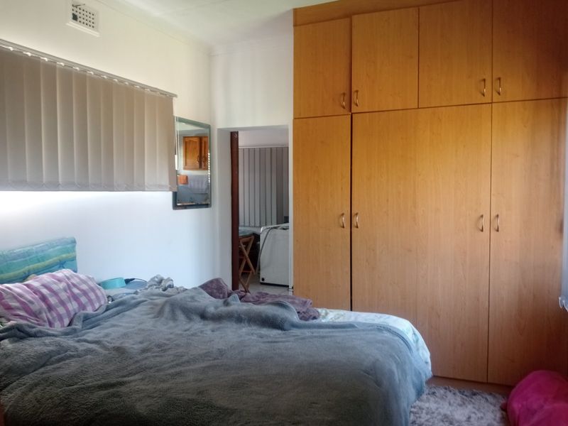 A bedroom featuring floor-to-ceiling built-in wooden cupboards and vertical window blinds, offering functional storage and natural light control.
