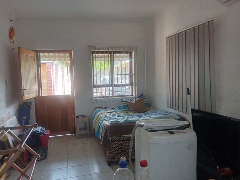 A bedroom featuring tiled flooring, vertical blinds, and a wooden exterior door with security bars on the window.