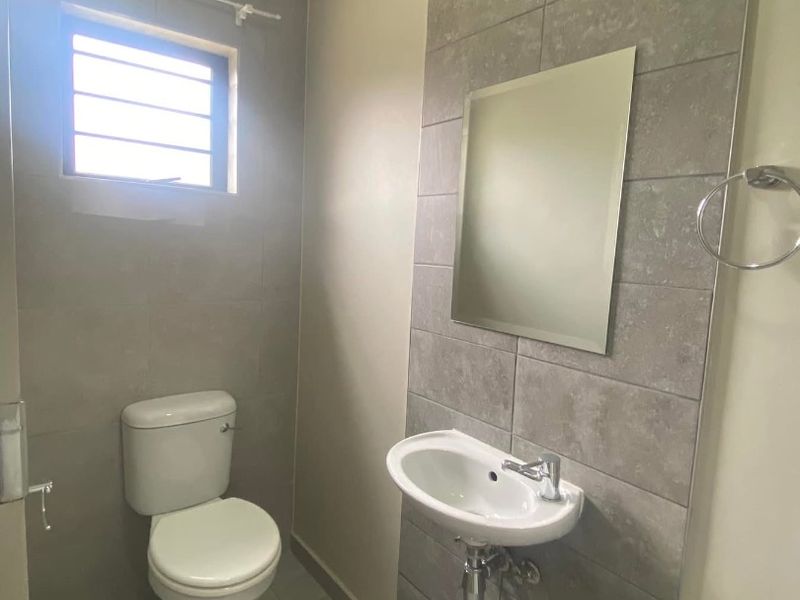 A clean and modern guest bathroom featuring a wall-mounted basin, toilet, and stylish grey tiled feature wall.