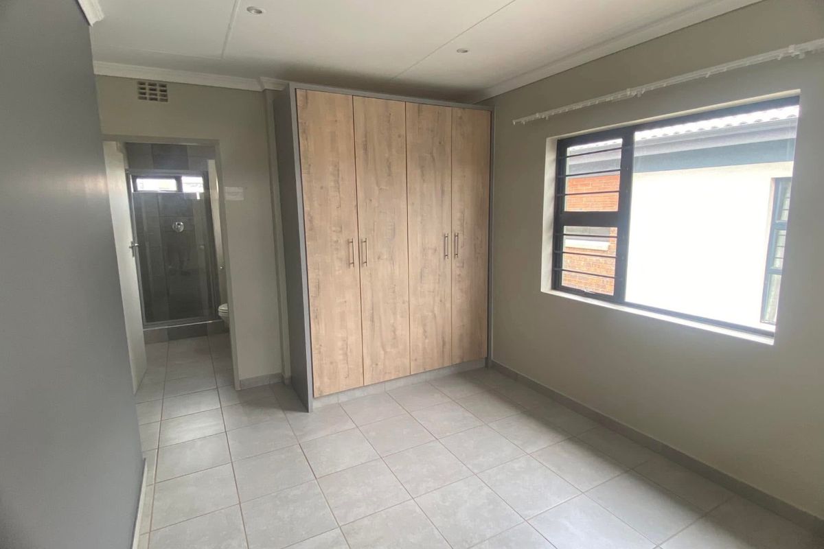A clean, empty bedroom featuring modern tiled flooring, a built-in wardrobe with wood-finish doors, and direct access to an en-suite bathroom.