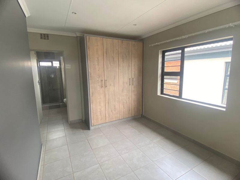 A clean, empty bedroom featuring modern tiled flooring, a built-in wardrobe with wood-finish doors, and direct access to an en-suite bathroom.