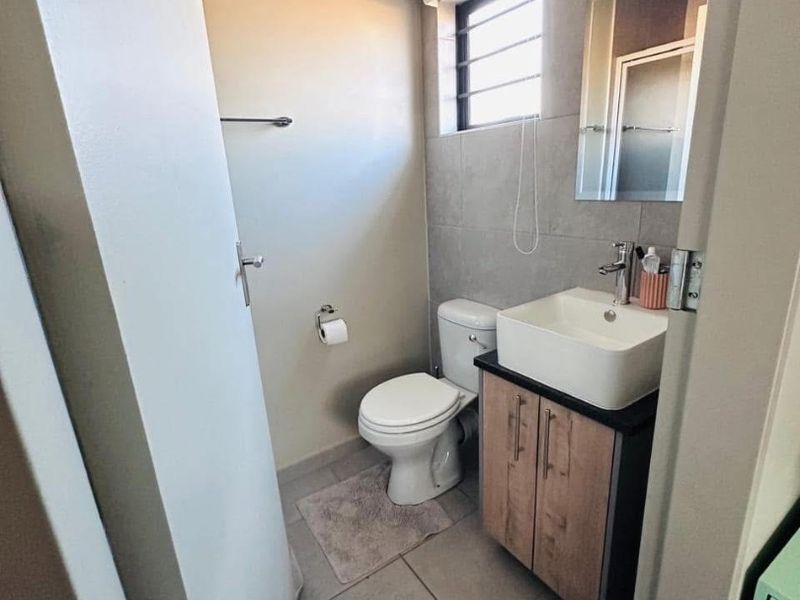 A modern, compact bathroom featuring a vessel sink vanity, tiled walls, and a louvered window for ventilation.