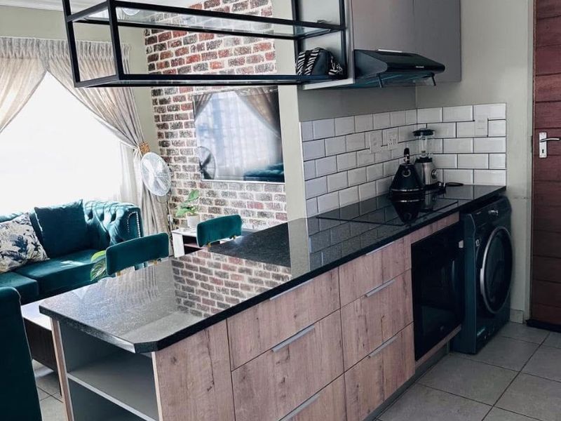 Modern open-plan kitchen featuring granite countertops, subway tile backsplash, and a striking exposed brick feature wall with integrated shelving.