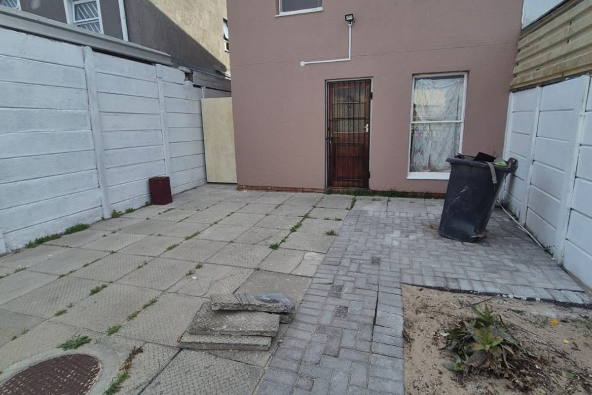 Rear exterior area featuring a paved patio, security gate, and precast concrete boundary walls, requiring maintenance and landscaping to improve the outdoor space.