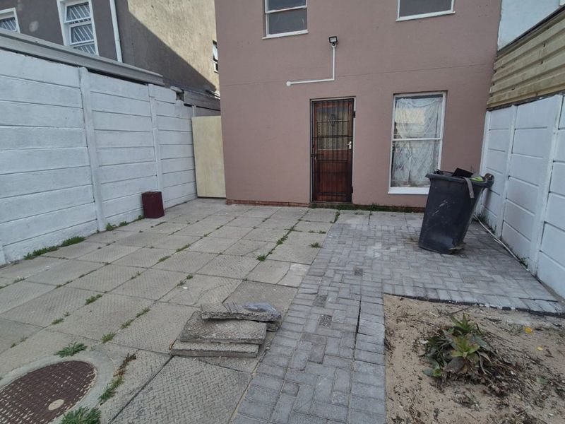 Rear exterior area featuring a paved patio, security gate, and precast concrete boundary walls, requiring maintenance and landscaping to improve the outdoor space.