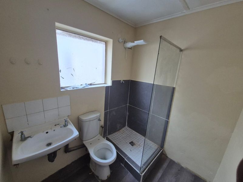 A functional bathroom featuring a pedestal basin, toilet, and a glass-enclosed shower with tiled splashbacks, requiring cosmetic updates to improve its overall condition.