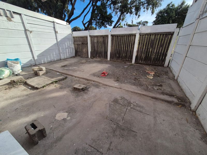 A rear outdoor area featuring a concrete slab base enclosed by precast concrete walls and weathered timber fencing, offering potential for landscaping or patio development.
