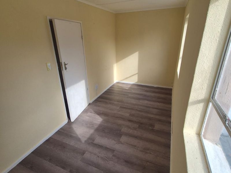 A clean, empty bedroom featuring modern laminate flooring, neutral wall paint, and natural light from the side window.