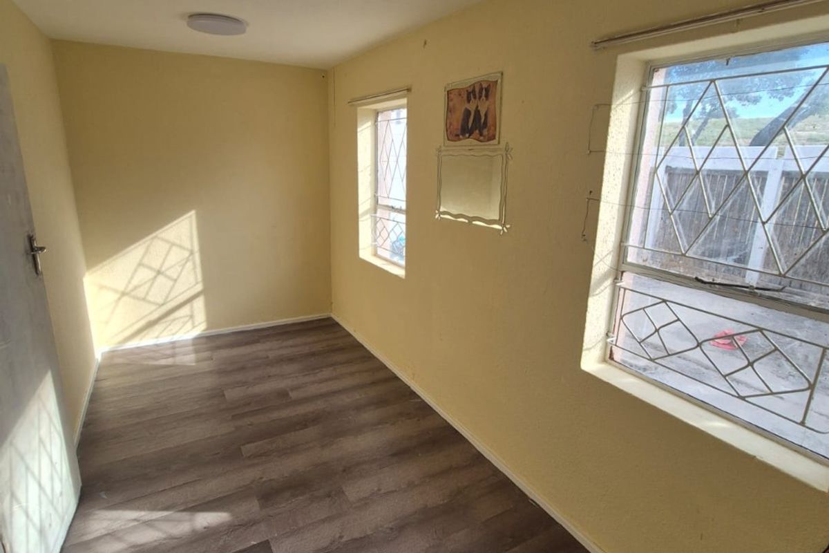 An empty bedroom featuring laminate flooring, security bars on windows, and a neutral wall finish, offering a blank canvas for potential updates.