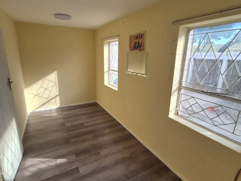 An empty bedroom featuring laminate flooring, security bars on windows, and a neutral wall finish, offering a blank canvas for potential updates.